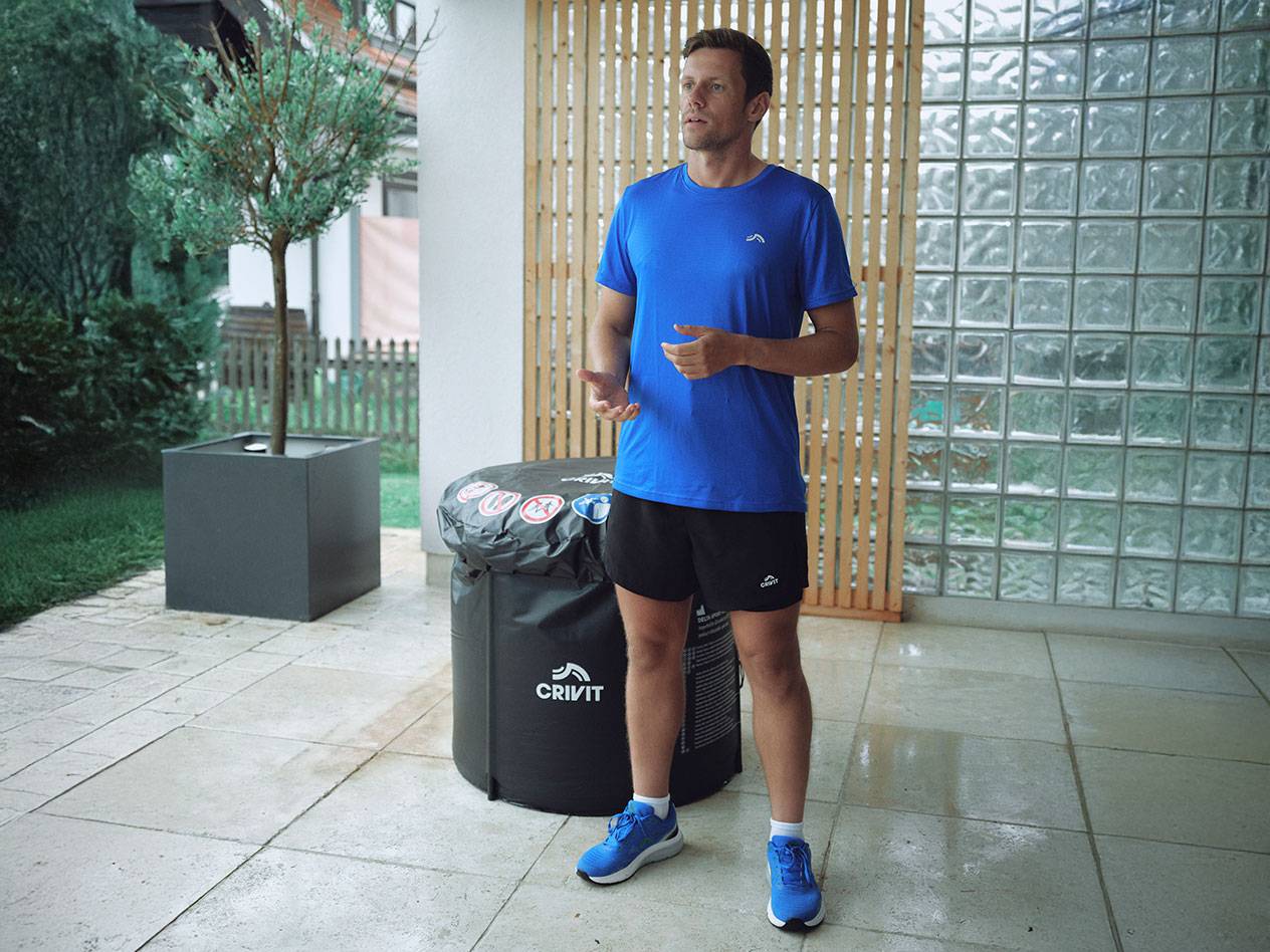 Man in Crivit activewear, blue t-shirt and black shorts, standing outdoors.