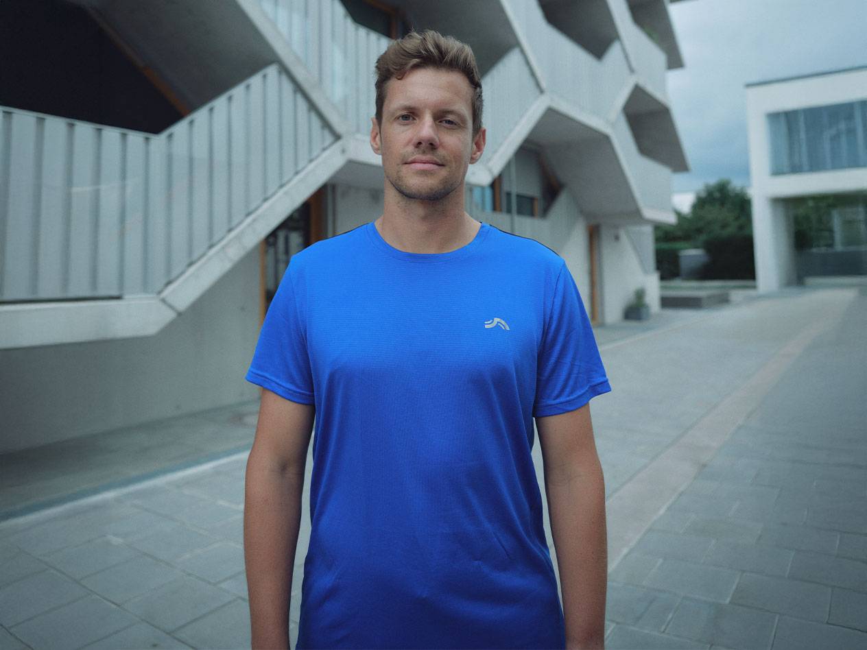 Man in blue Crivit sports t-shirt, with a modern building in the background.