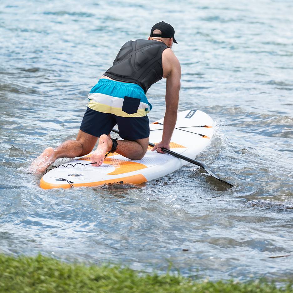 Man kneeling on a paddleboard with a paddle in the water.