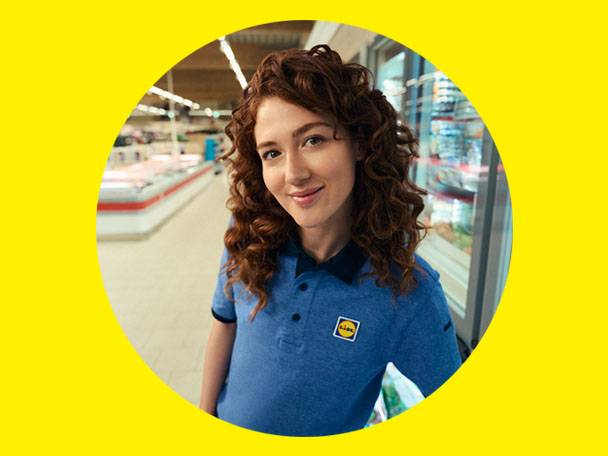 Smiling woman in a blue uniform with a Lidl logo in a grocery store.