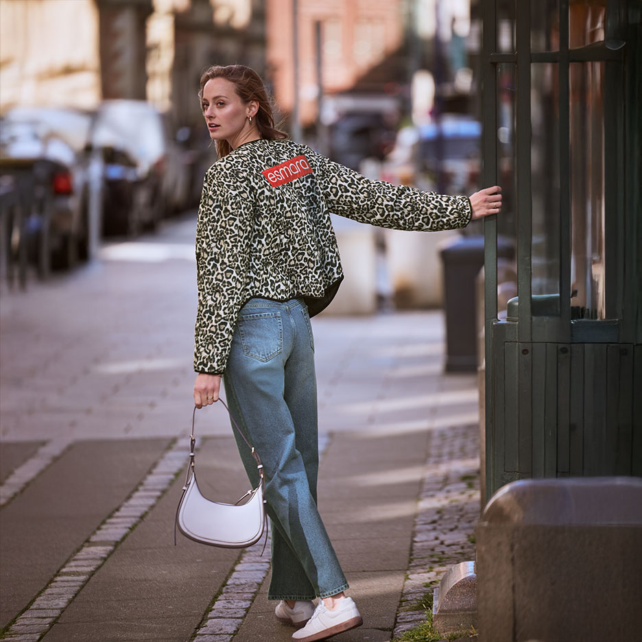 Woman in Esmara leopard print jacket and jeans, with a handbag, on a street.