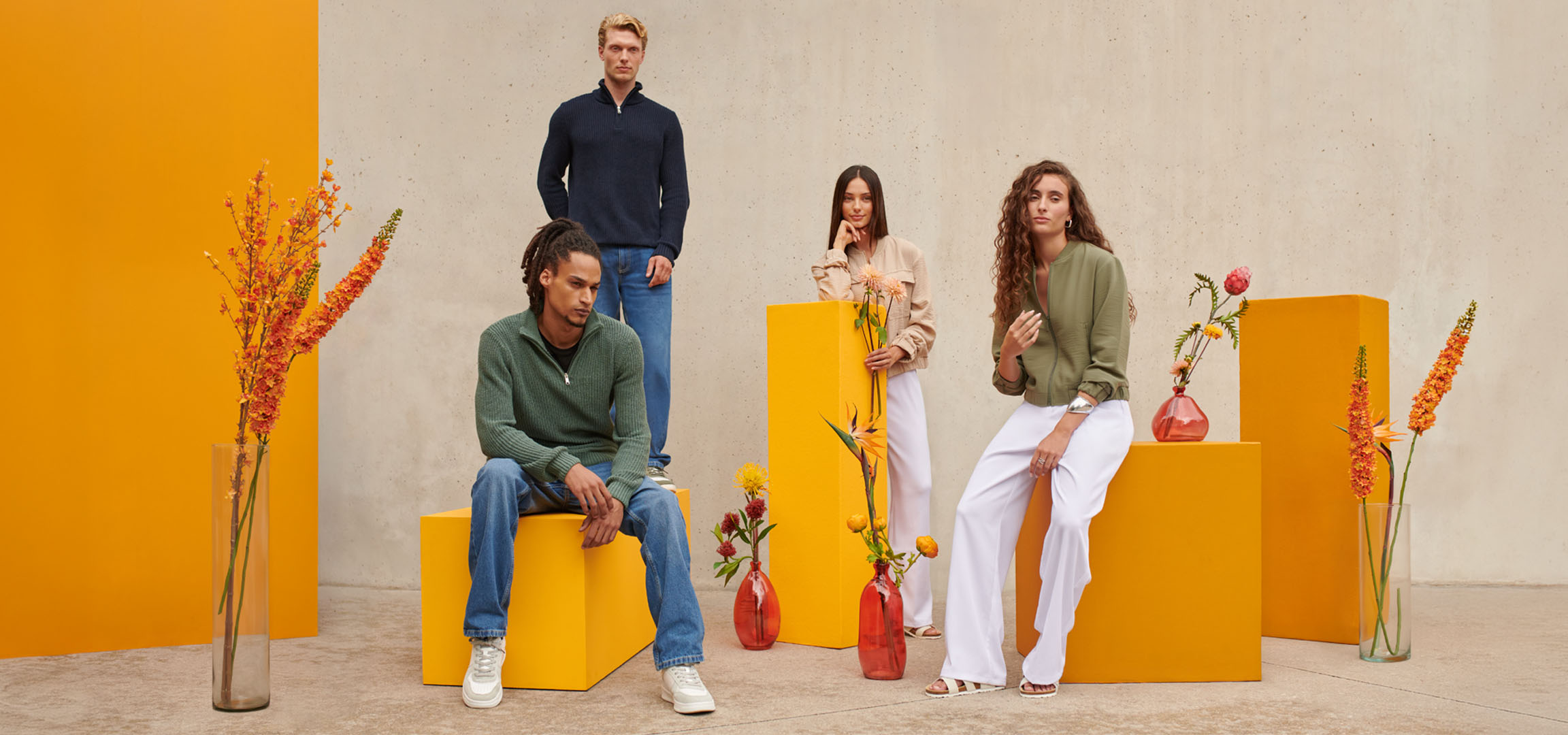 Four people in sweaters and jeans, sitting and standing against orange blocks.