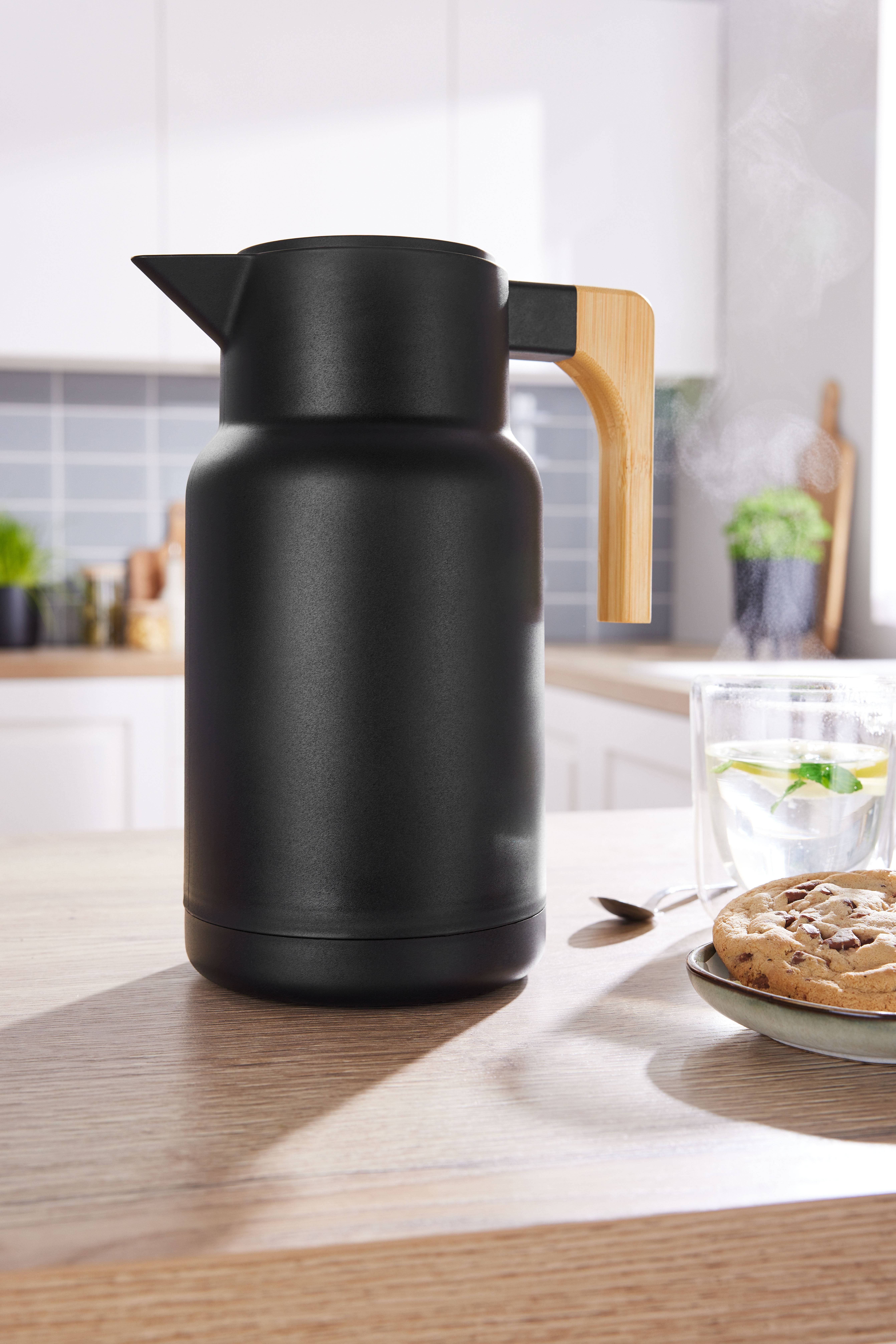 Black thermos flask with a wooden handle on a kitchen table with biscuits and tea.