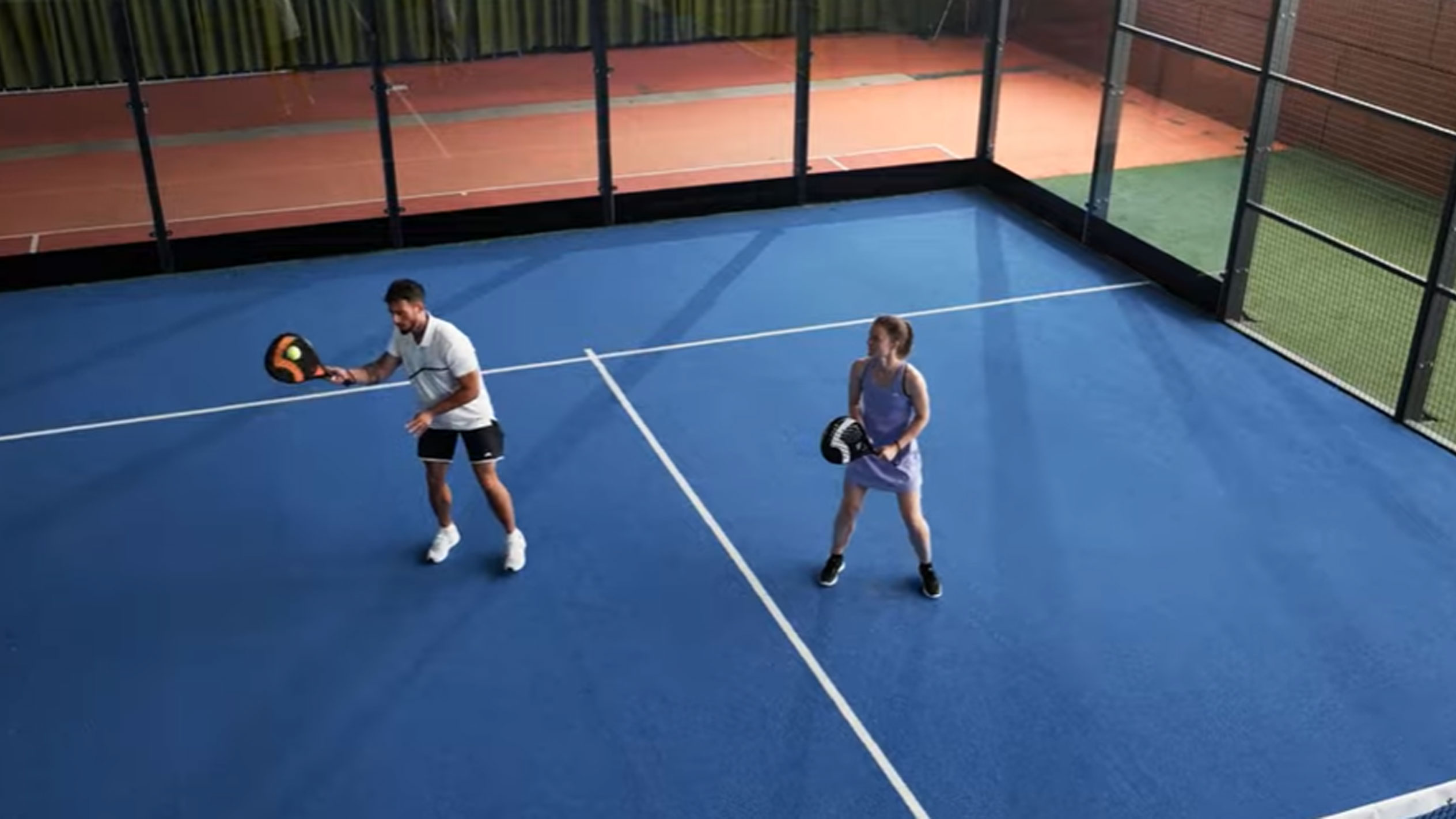 Man and woman playing padel on blue court with rackets and ball