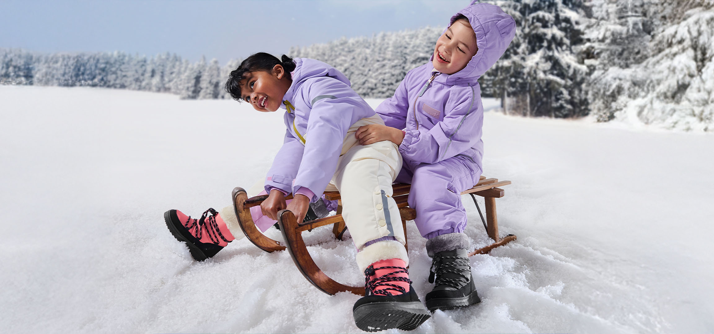 Two children in purple snowsuits and winter boots sledding in a snowy landscape.