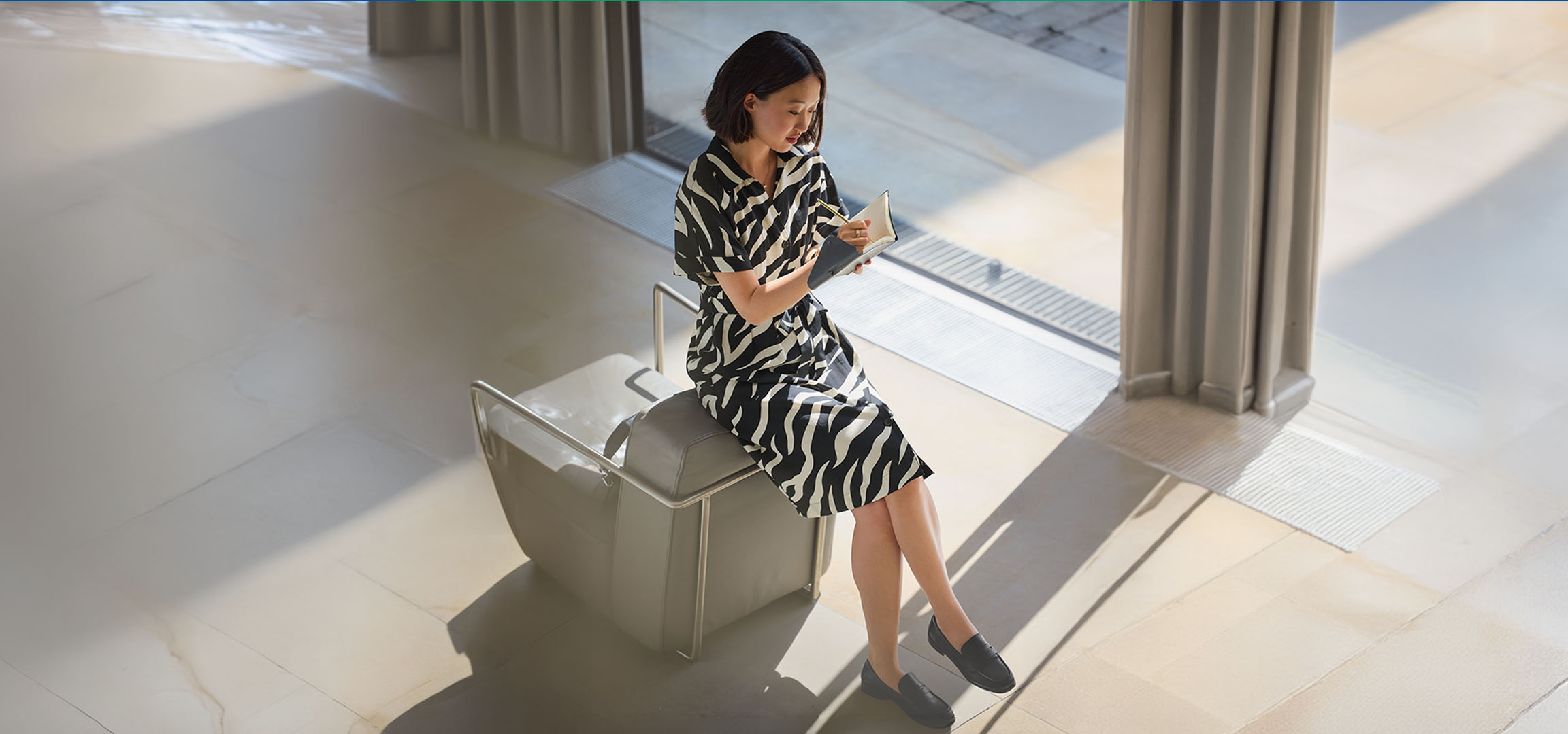 Woman in a zebra print dress, sitting on a chair, writing in a notebook.