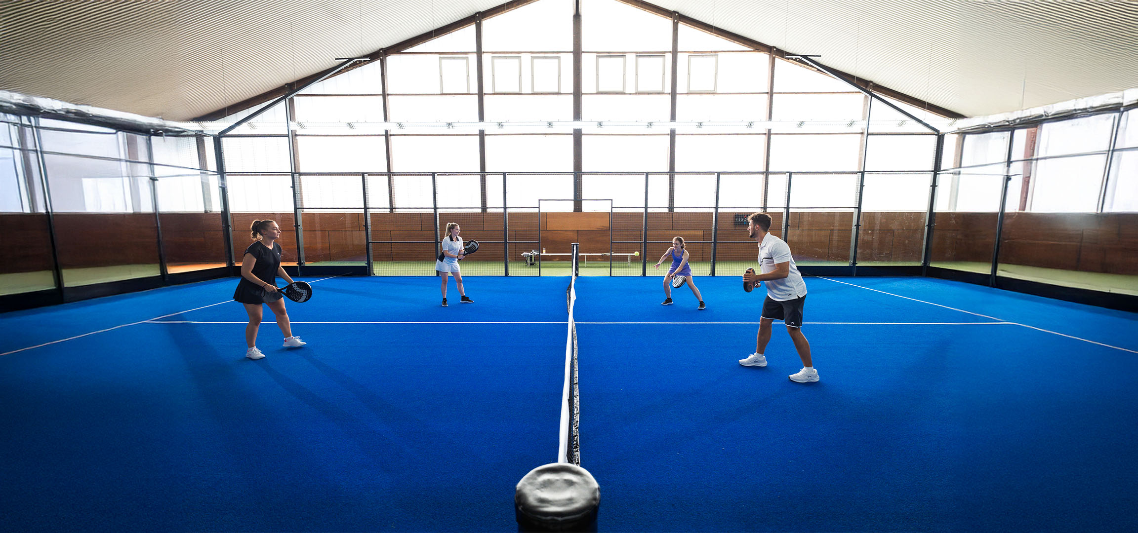 Four people play padel on a blue court, with rackets and sportswear.
