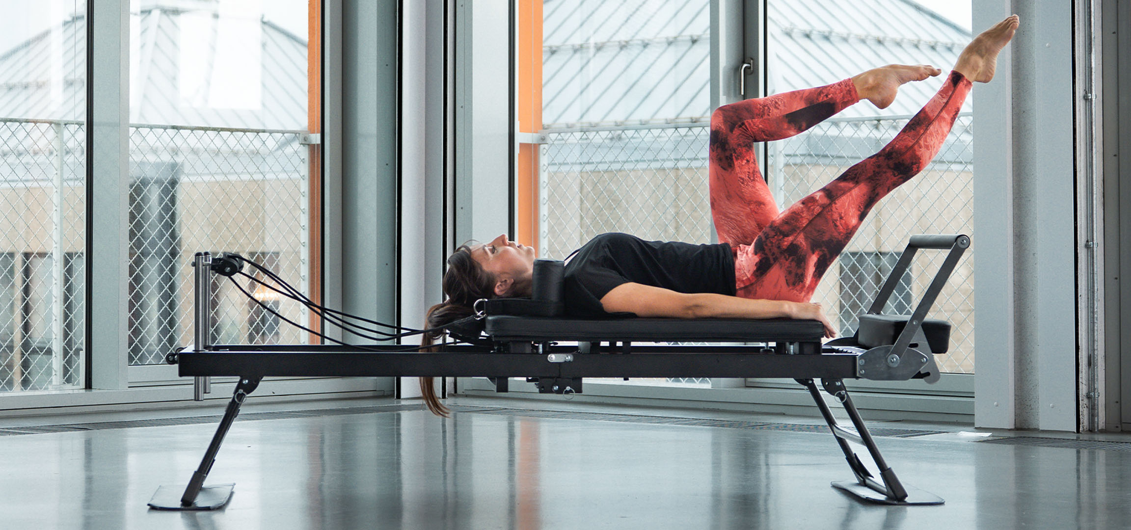 Woman doing Pilates on a reformer machine, with fitness accessories nearby.