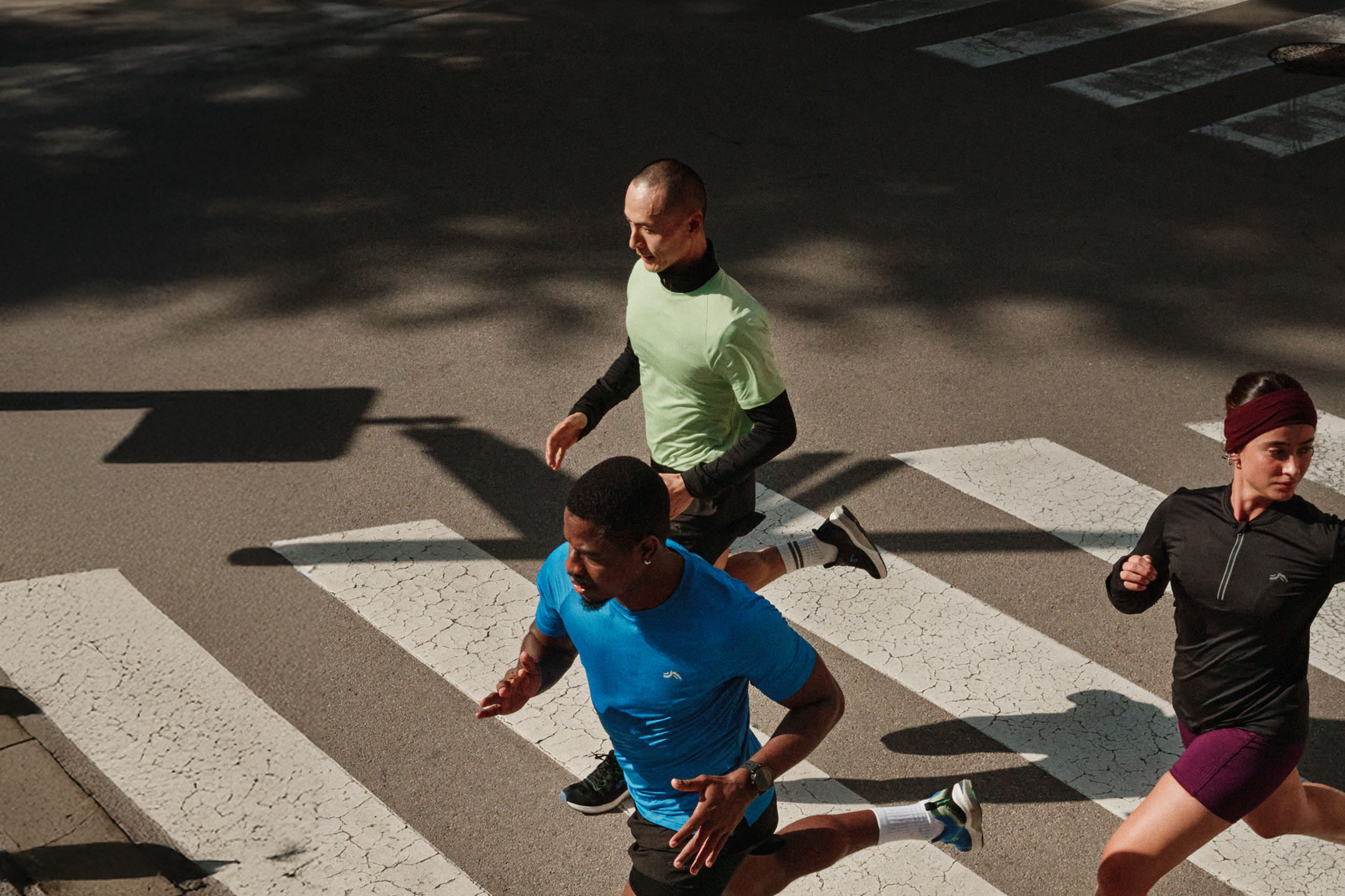 Three runners in sportswear crossing a pedestrian crossing in the city.