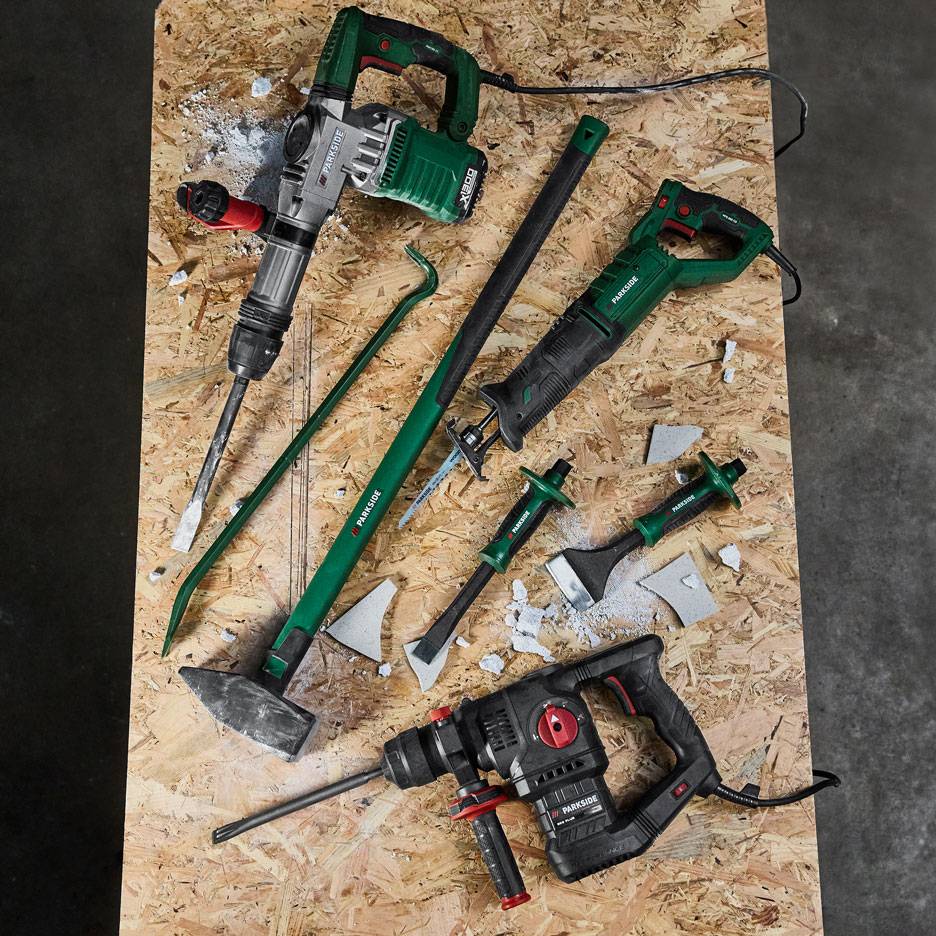 Collection of power tools and hand tools for demolition and construction work on a wooden surface.
