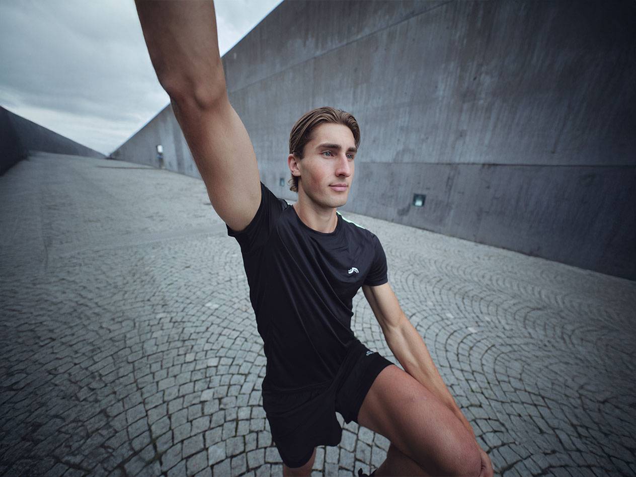 Man in black Crivit sports T-shirt and shorts stretching outdoors.