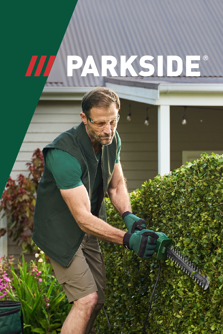 Man trimming a hedge with an electric hedge trimmer, wearing safety glasses and gloves.