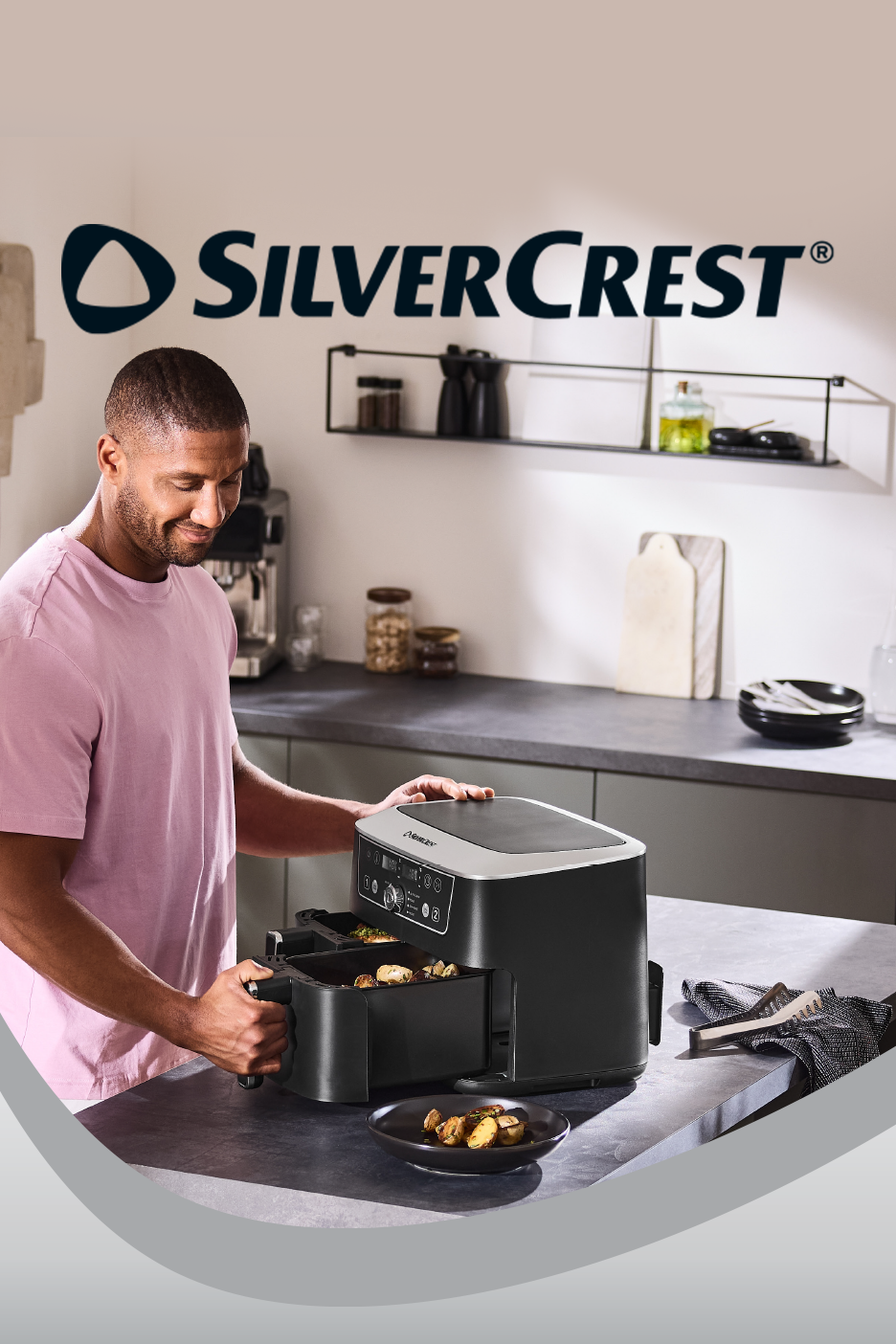 Man using a black dual-basket air fryer to serve roasted potatoes in a modern kitchen.