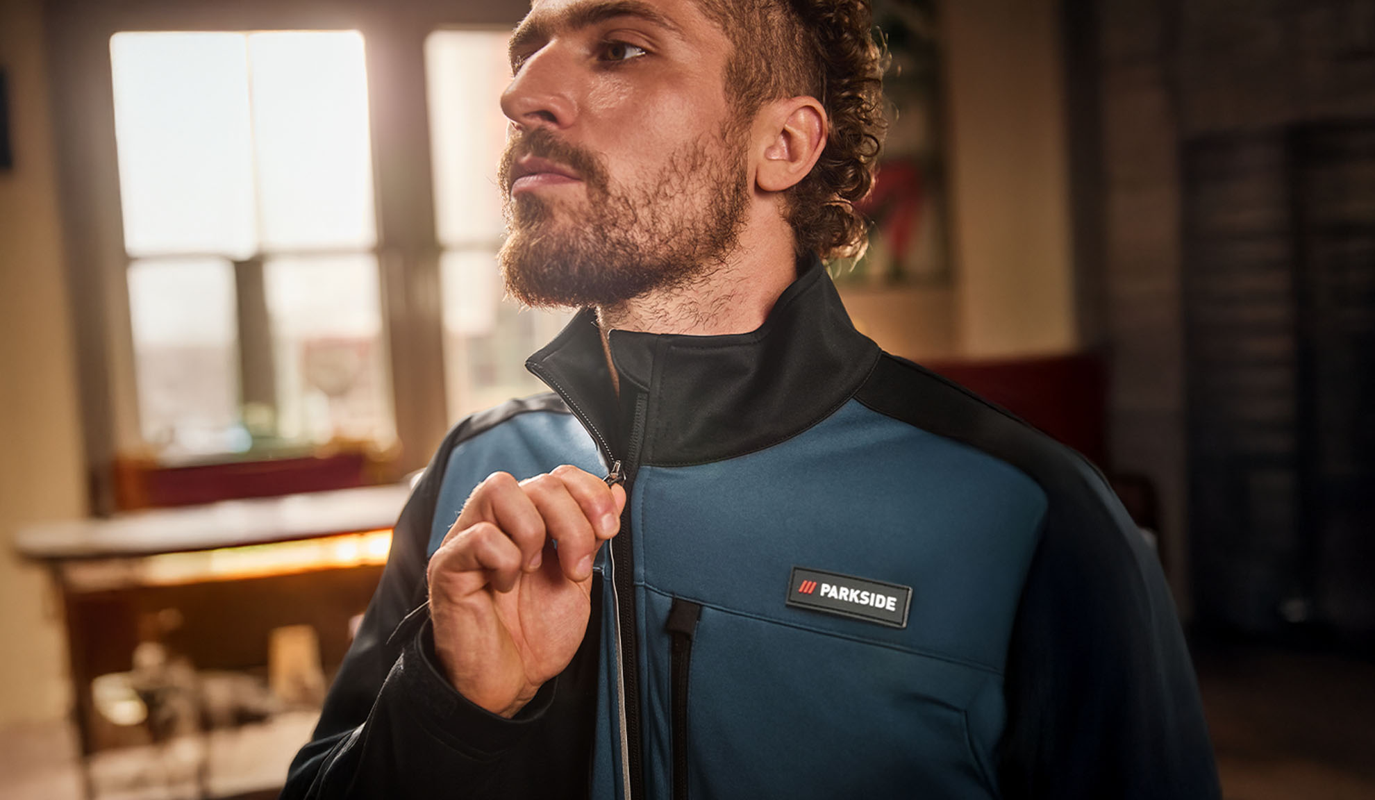 Man in a blue and black Parkside work jacket, zipping it up.