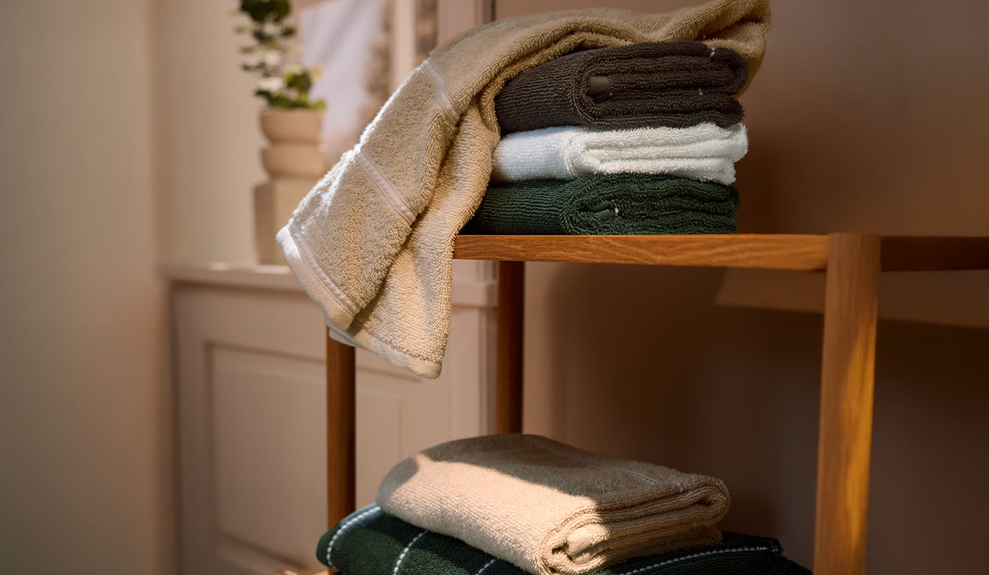 Bath towels in neutral and green colors stacked on a wooden shelf.