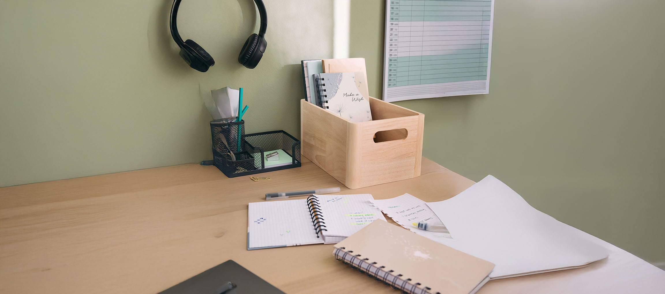 Desk with headphones, mesh organizer, wooden box, and notebooks.