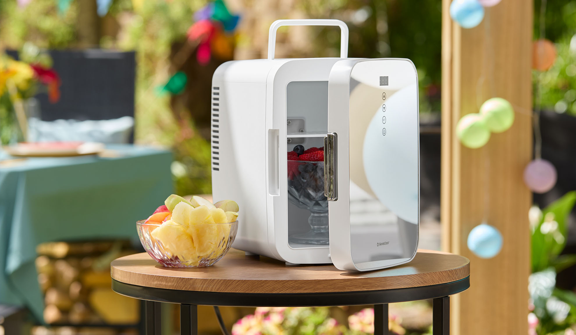 Portable mini fridge with fruit on a wooden table outdoors.