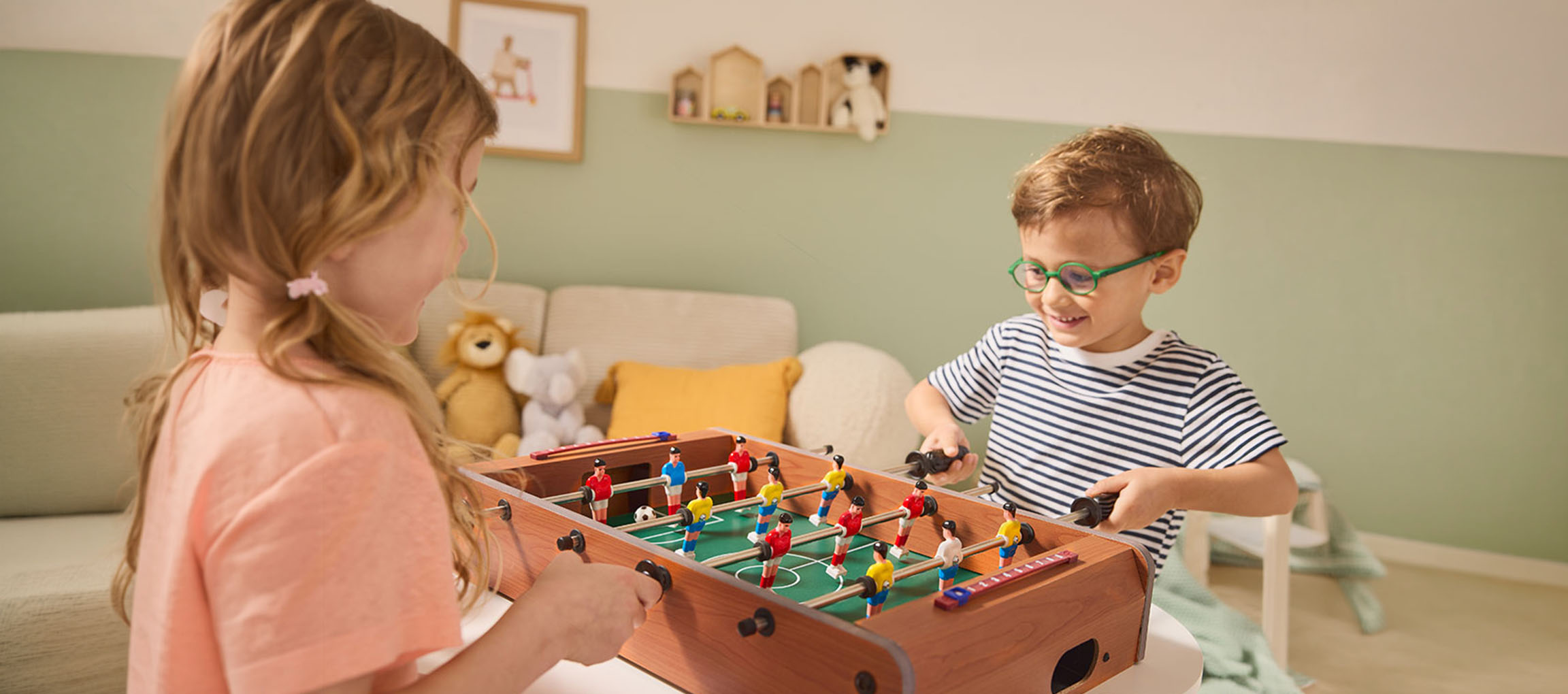 Two children playing table football, a girl in a pink shirt and a boy in a striped shirt.
