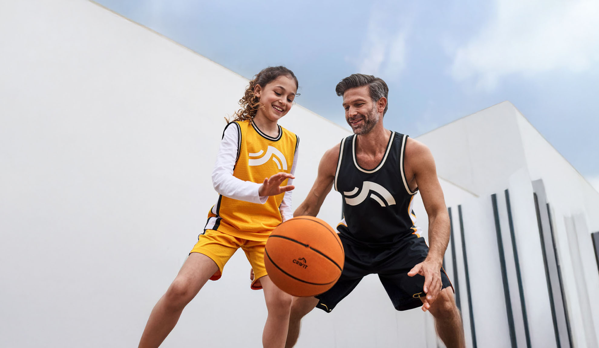 Father and daughter playing basketball in Crivit jerseys and shorts.