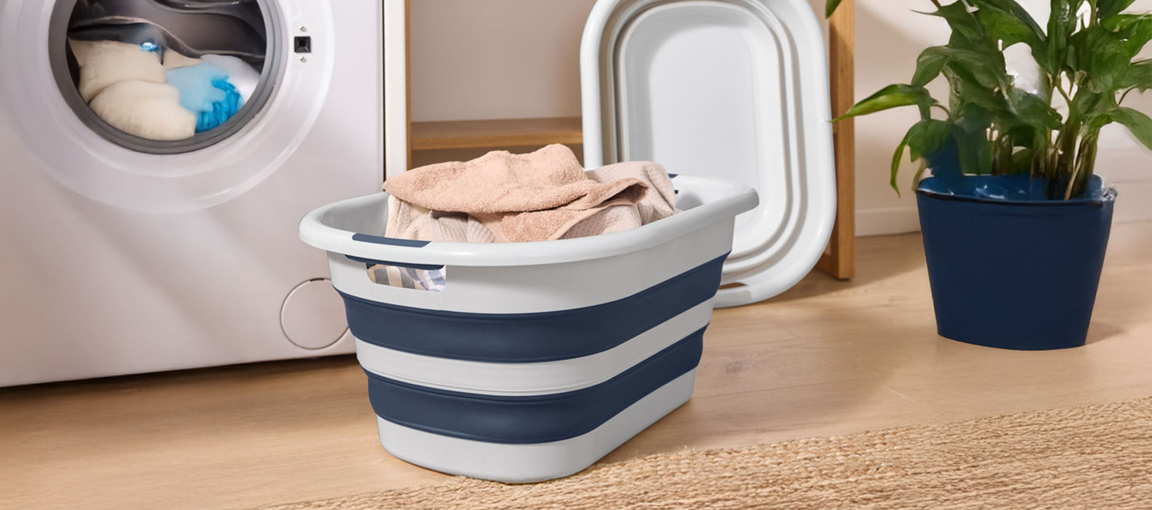 A white washing machine with a blue and white collapsible laundry basket filled with towels.