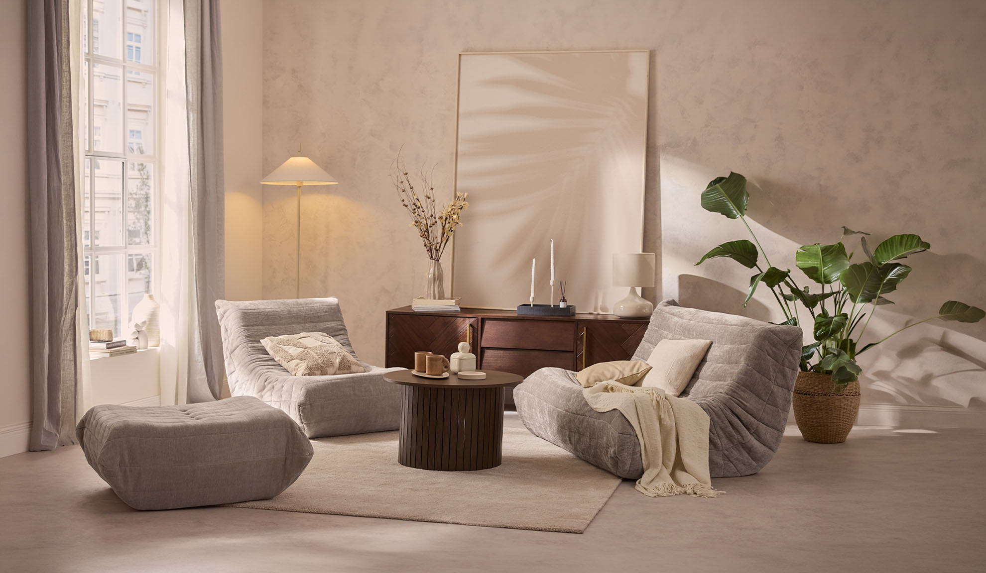 Cozy living room with two grey lounge chairs, an ottoman, a coffee table, and a plant.