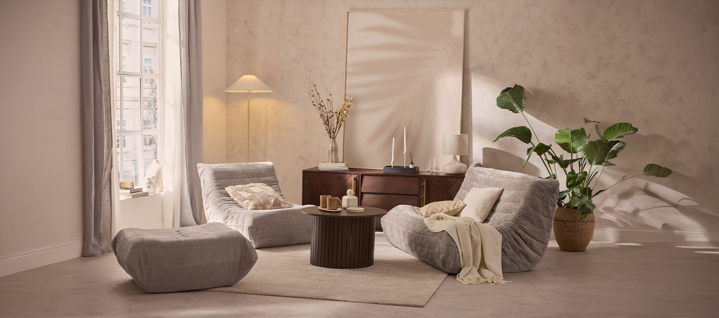 Cozy living room with two grey lounge chairs, an ottoman, and a wooden table.