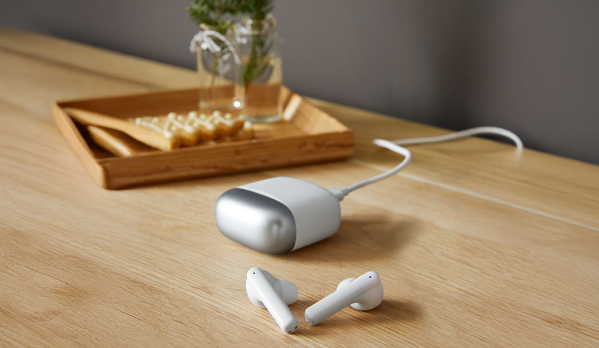 White earbuds and a charging device on a wooden table.