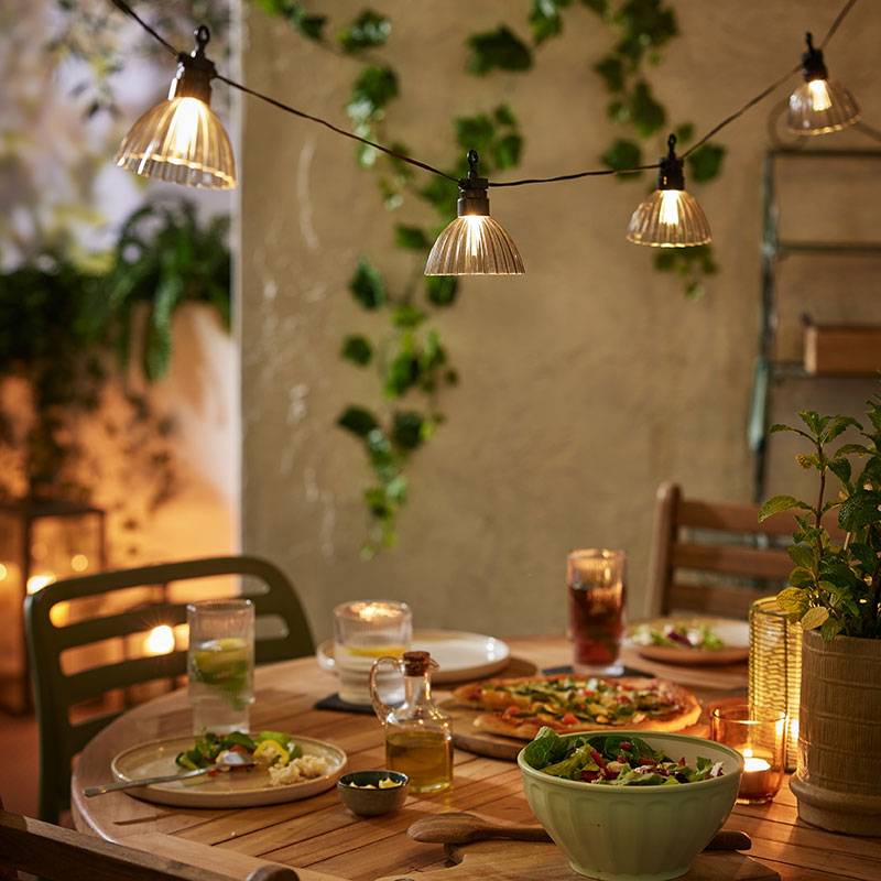 Outdoor string lights with warm lights above a wooden table with food.