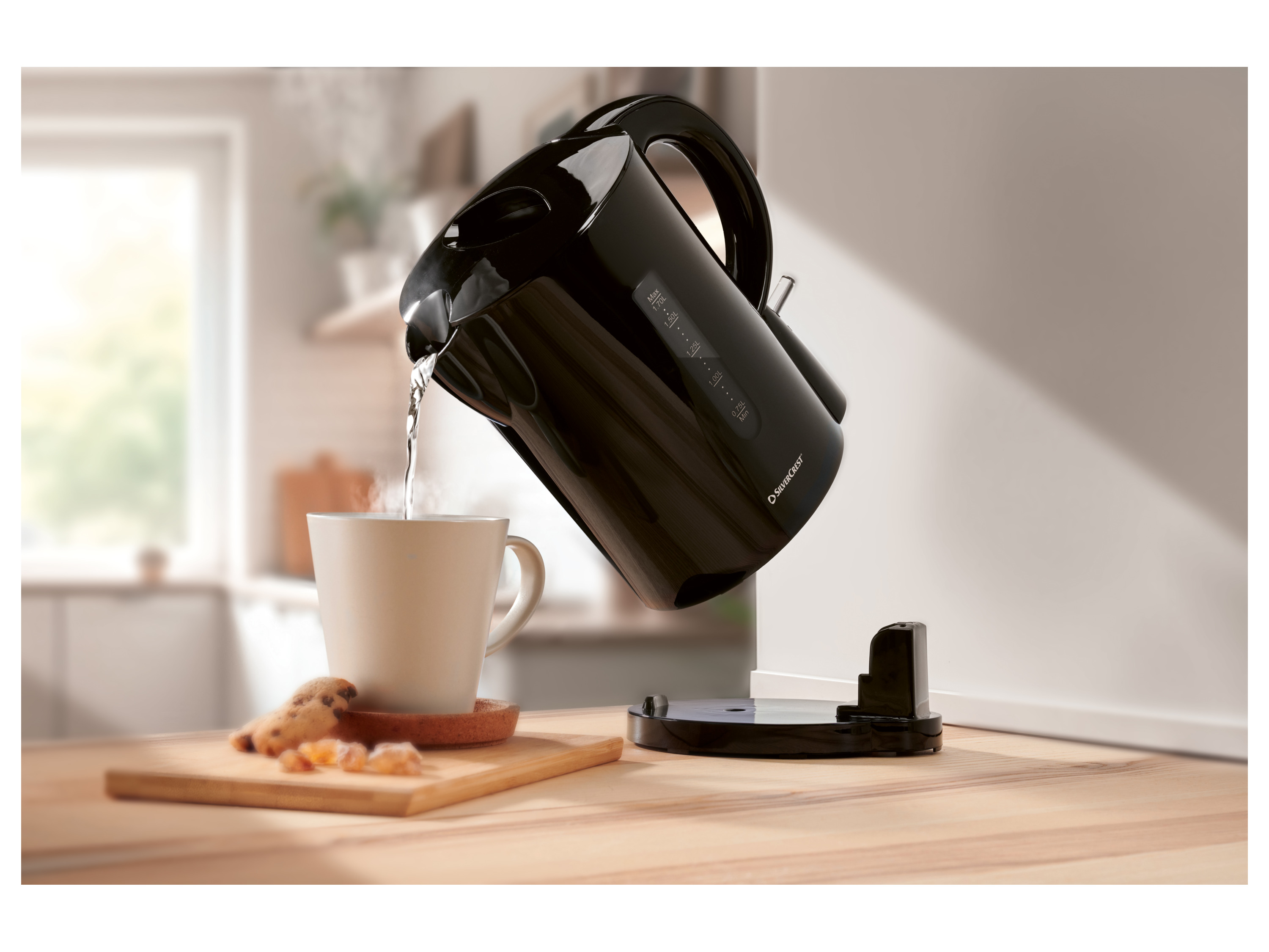 Black Silvercrest kettle pouring hot water into a mug on a wooden table.