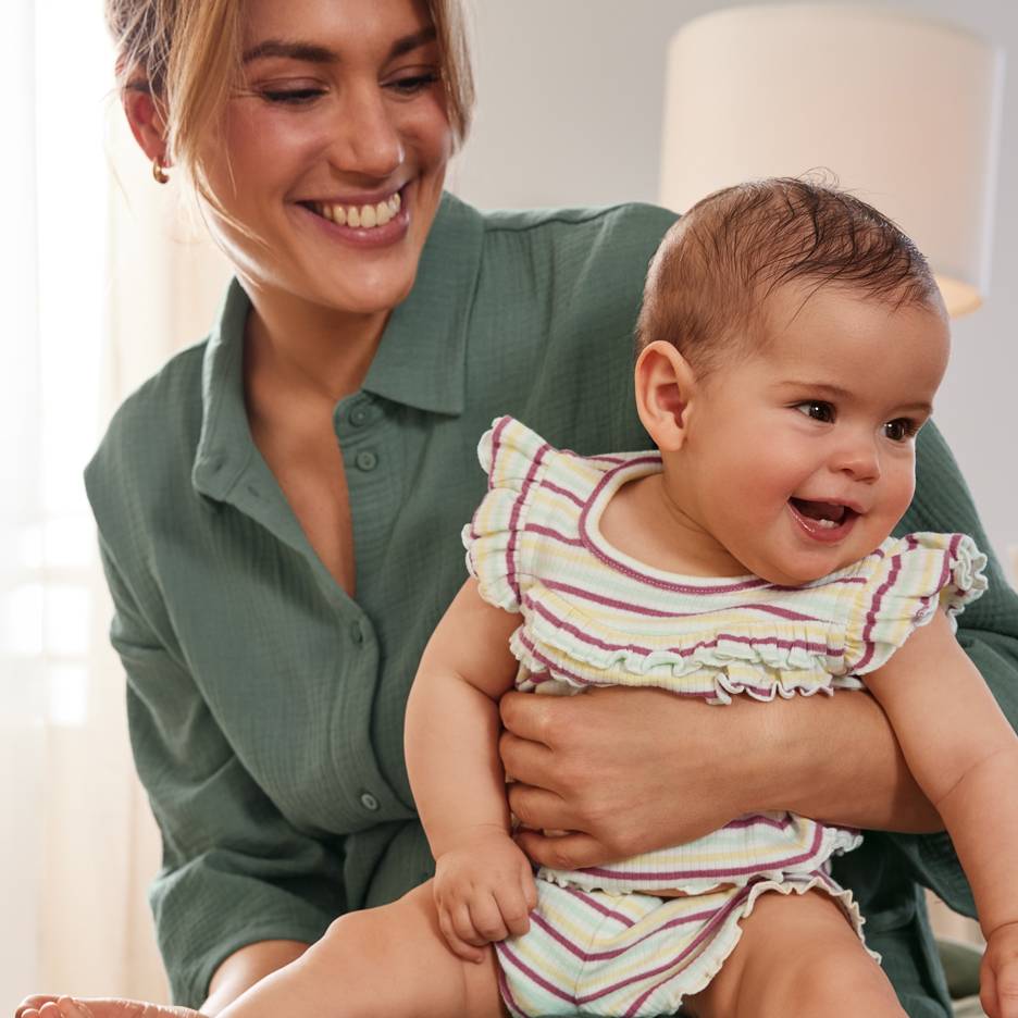 Smiling mother with a happy baby wearing a colorful striped outfit.