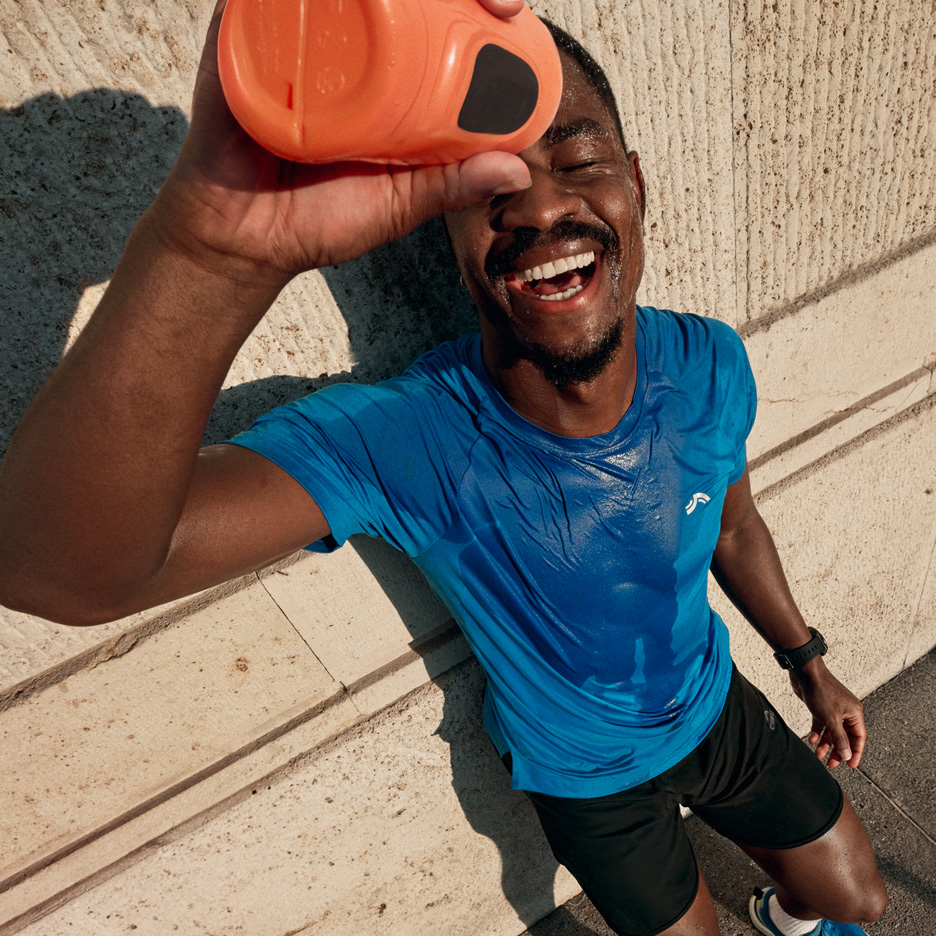 Man in blue sports t-shirt and black shorts pouring water on himself after workout.