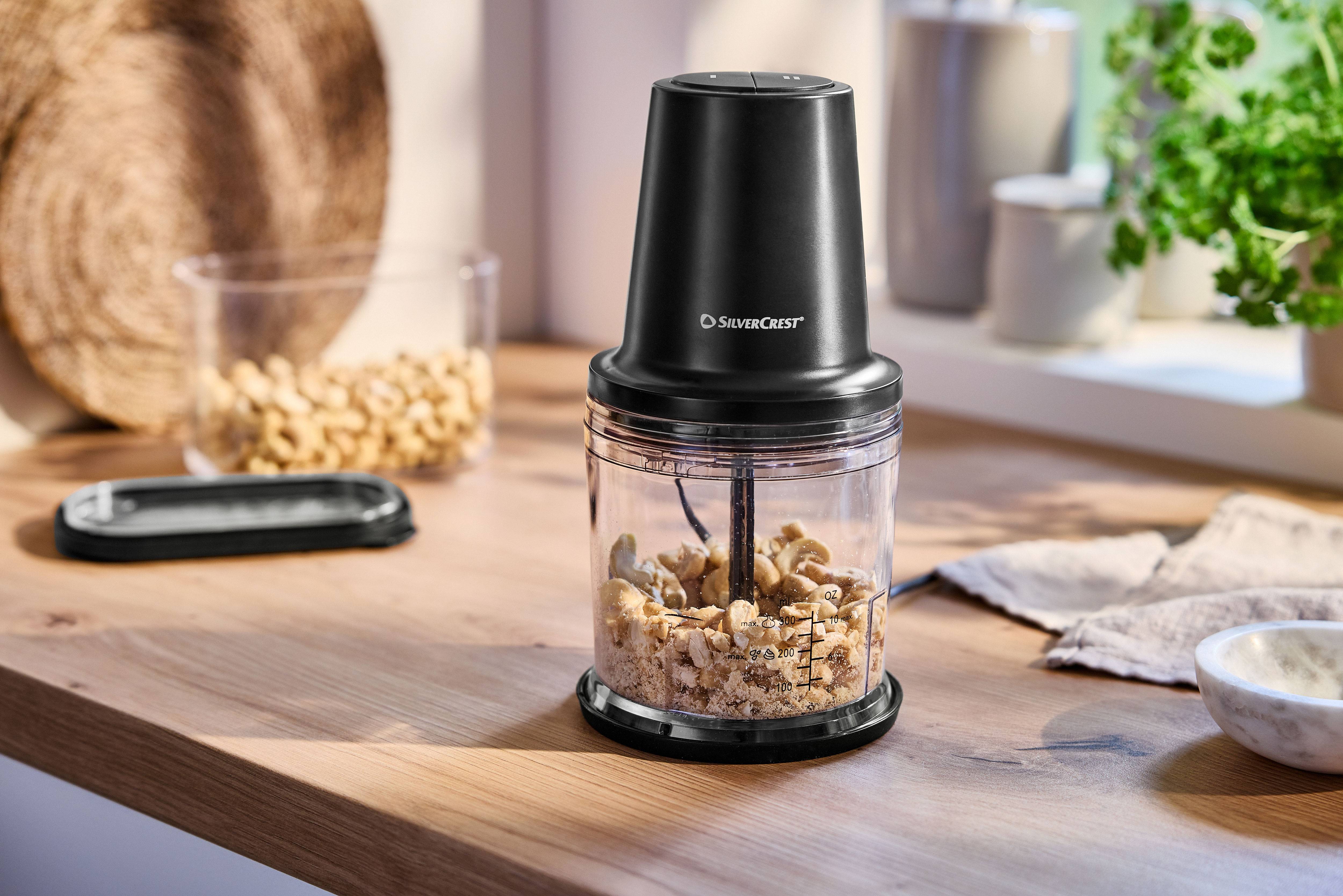 Black chopper with cashews on a wooden kitchen countertop.