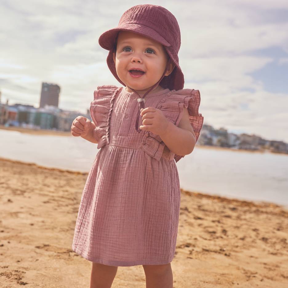 Baby in pink dress and hat on the beach.